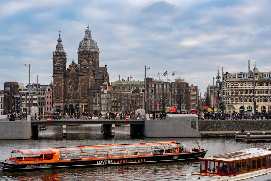 Scenic view of the Basilica of Saint Nicholas alongside Amsterdam's canal, featuring a tour boat.