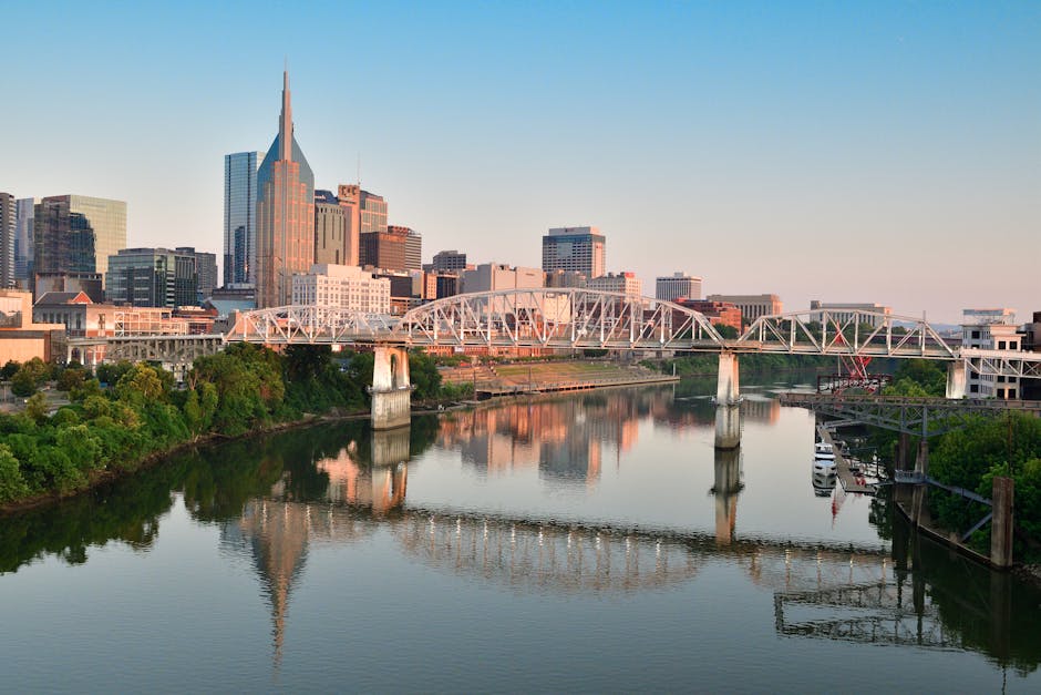 Scenic view of Nashville skyline and pedestrian bridge reflecting in the Cumberland River at sunrise.