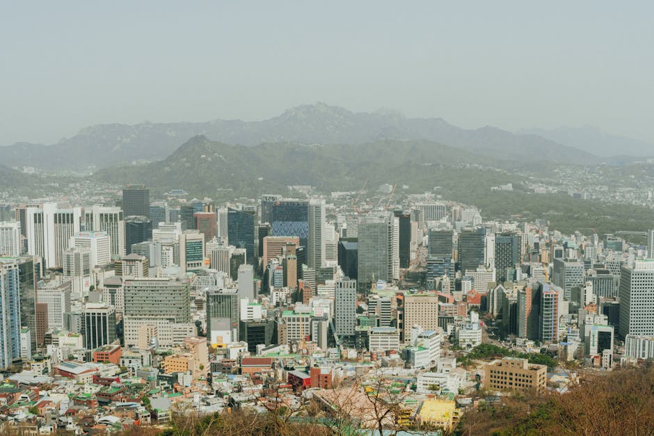 Panoramic aerial view of Seoul's skyscrapers with surrounding mountains, depicting modern urban landscape.