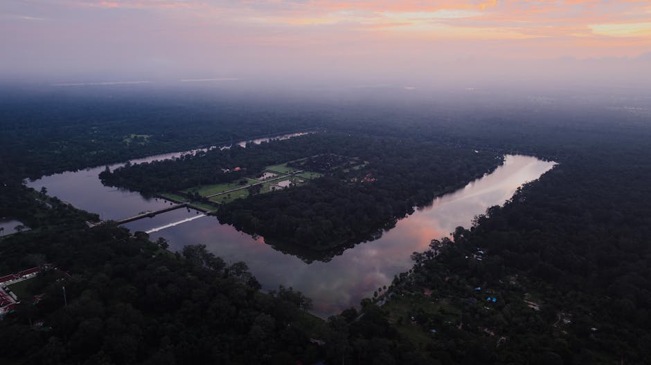 A breathtaking aerial view of Angkor Wat surrounded by lush forest at sunset, reflecting water bodies in Krong Siem Reap, Cambodia.